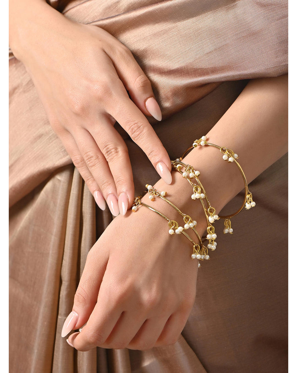 A gold-plated white pearl bangle worn on a person's wrist, featuring a slip-on closure and ornamental pearl drops.