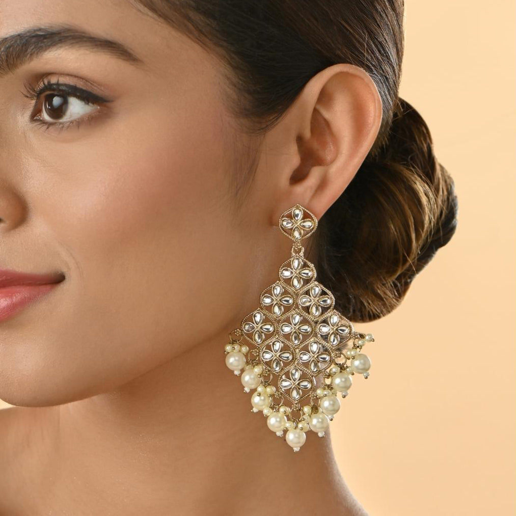 A woman wearing white kundan stone drop earrings with a traditional design.