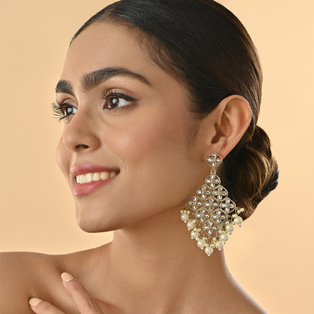 A woman wearing white kundan stone drop earrings with a traditional design.