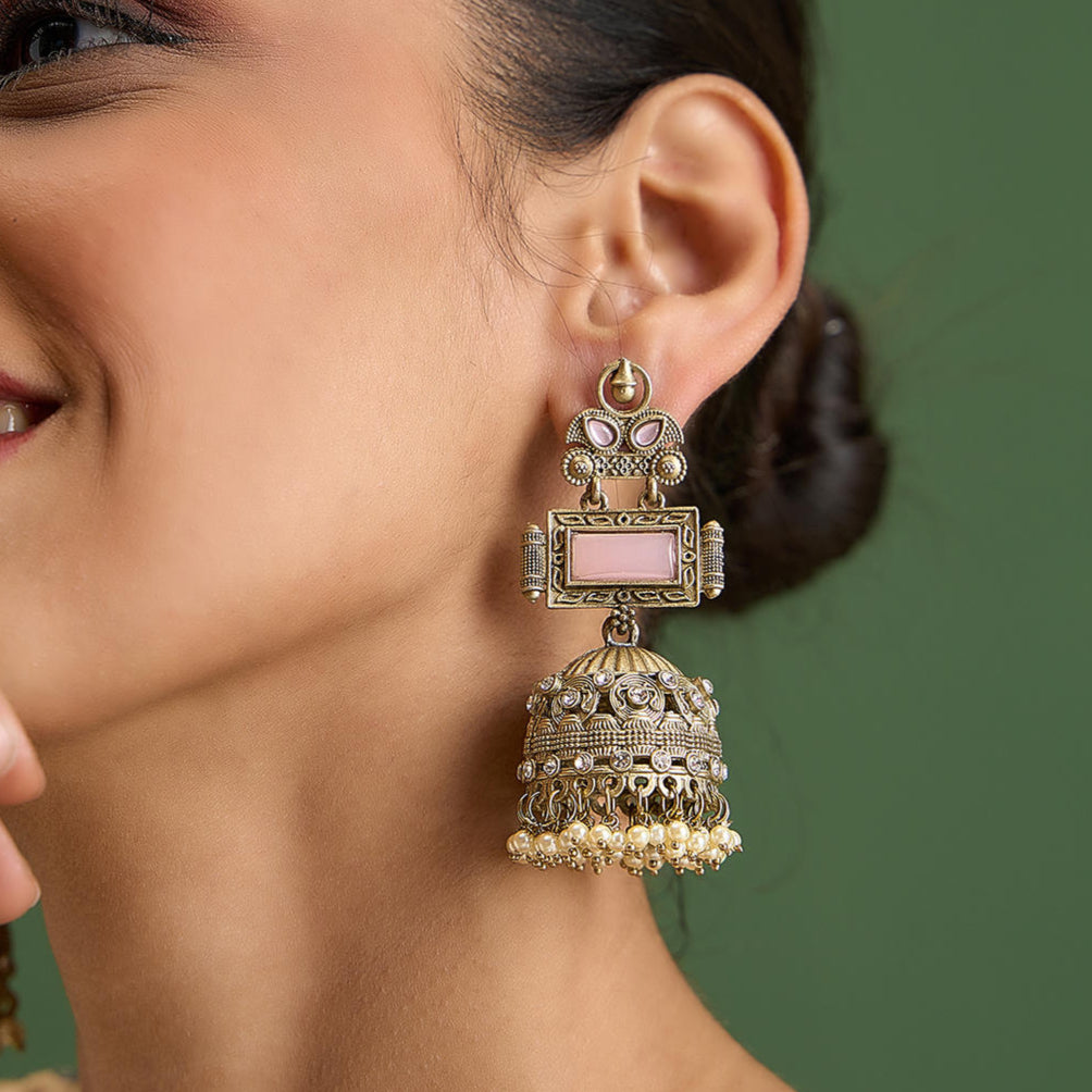 A woman wearing oxidised silver jhumkas earrings with baby pink stones and white pearls.
