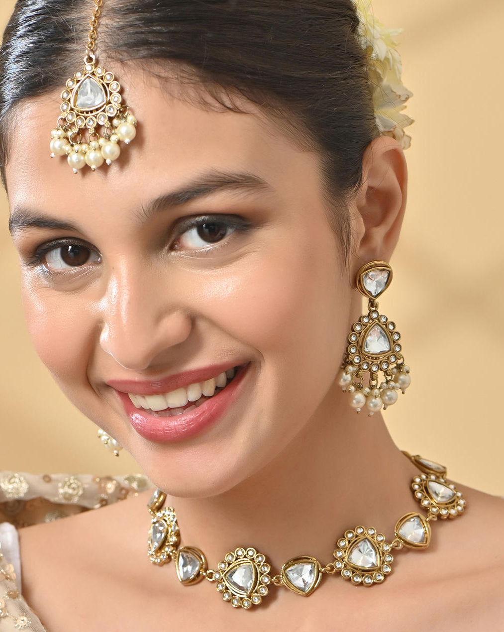 A woman wearing a bridal necklace, earrings, and a maang tikka with white pearl and gold studs.