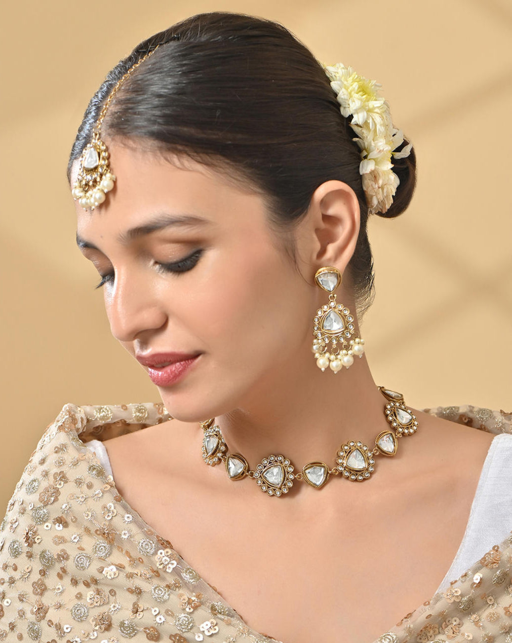 A woman wearing a bridal necklace, earrings, and a maang tikka set with white pearl and kundan studded in gold-plated designs.