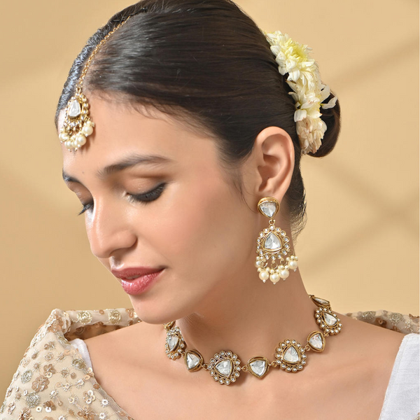 A woman wearing a bridal necklace, earrings, and a maang tikka set with white pearl and kundan studded in gold-plated designs.