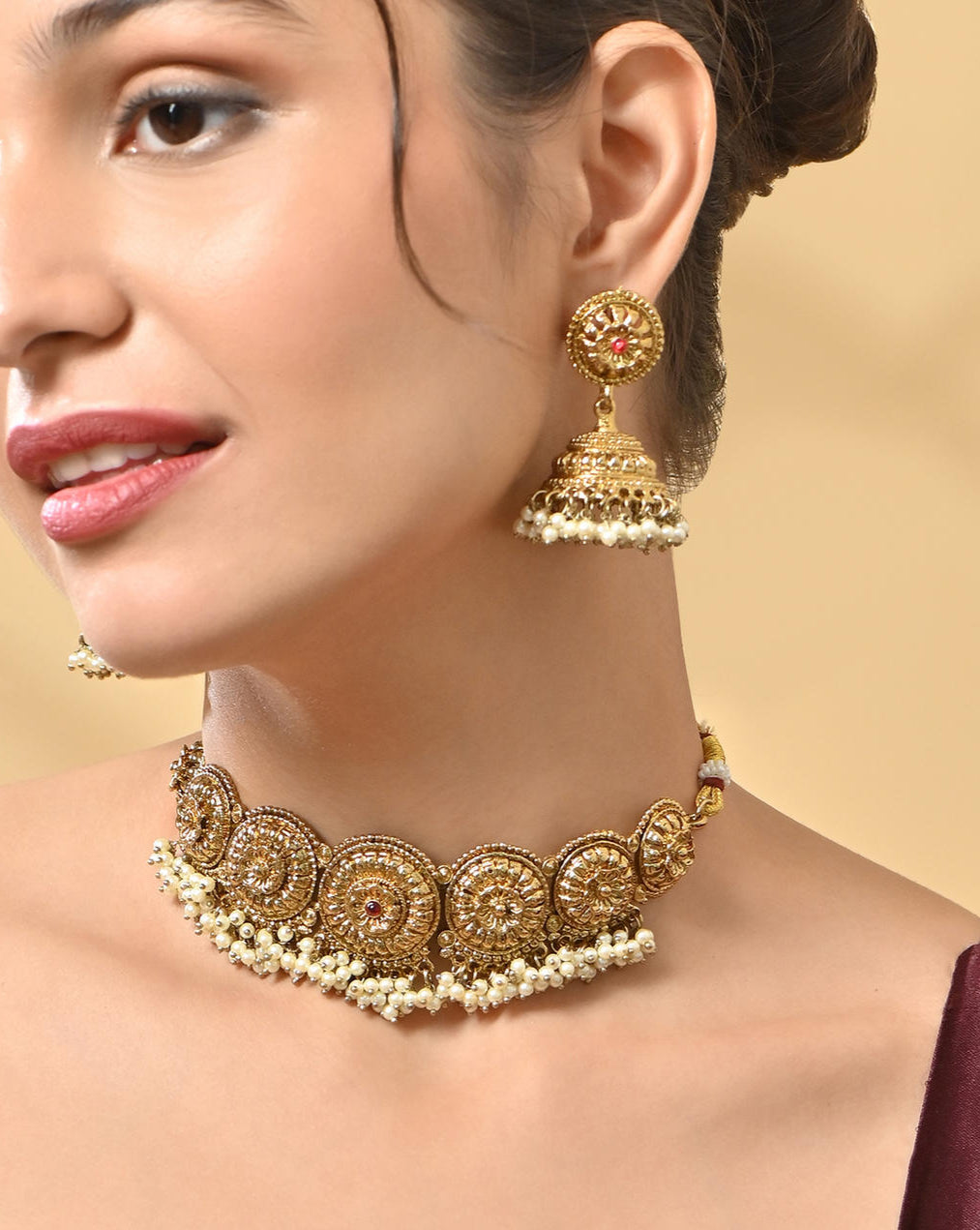 A woman wearing a mehendi gold temple necklace and earrings set with intricate designs and pearl accents.