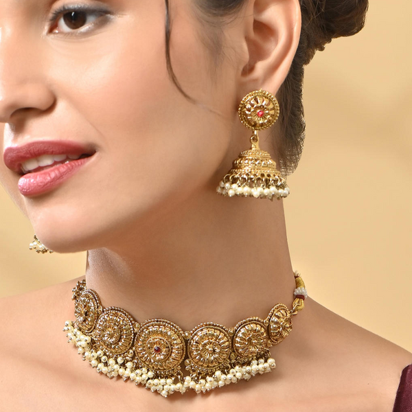 A woman wearing a mehendi gold temple necklace and earrings set with intricate designs and pearl accents.
