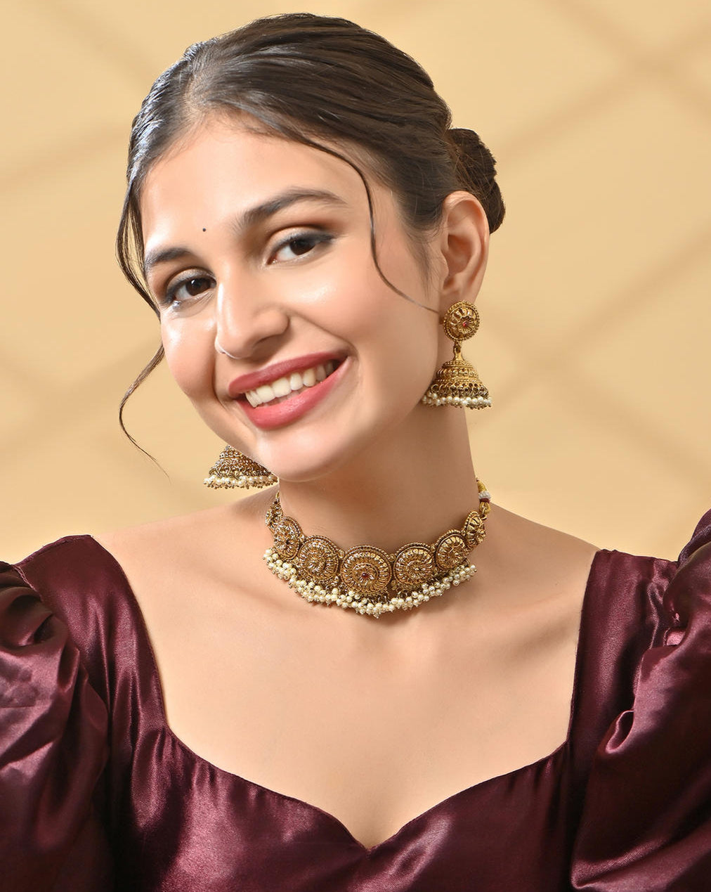 A woman wearing a mehendi gold temple necklace and earrings set with intricate designs and pearl accents.