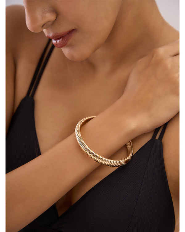 A person wearing a black dress and a gold coiled cuff bracelet with gold accents on their wrist.