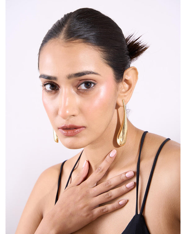 A woman wearing gold-plated long teardrop earrings with a molten finish.