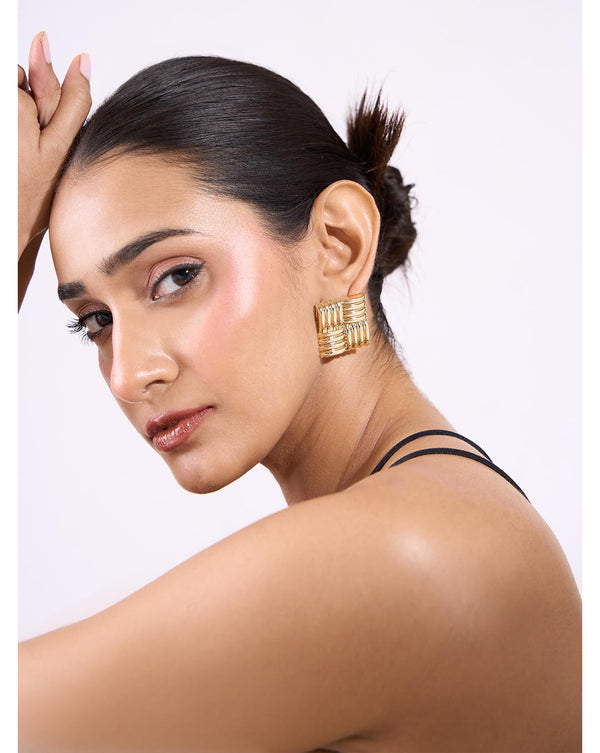 A woman wearing gold square textured party stud earrings from the brand Toniq. The earrings are gold-plated and have a textured finish.