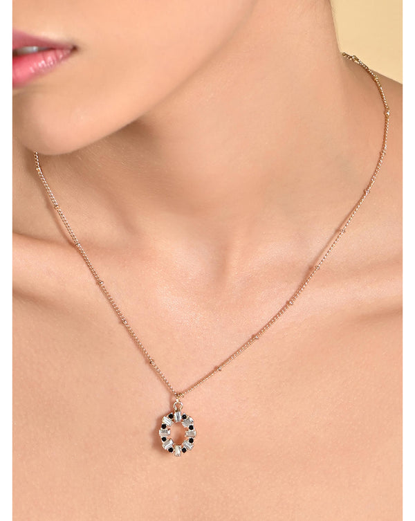 A sleek circular pendant necklace with black and white cubic zirconia stones suspended on a gold-toned chain.
