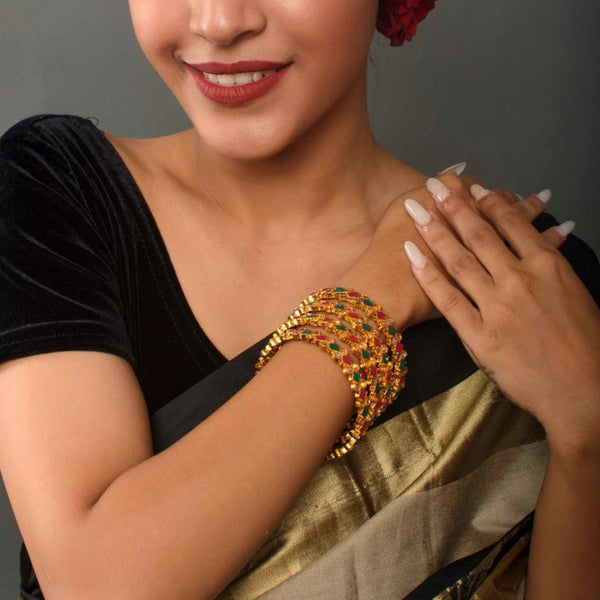 A woman wearing a gold and multicolor stone bracelet on her wrist.