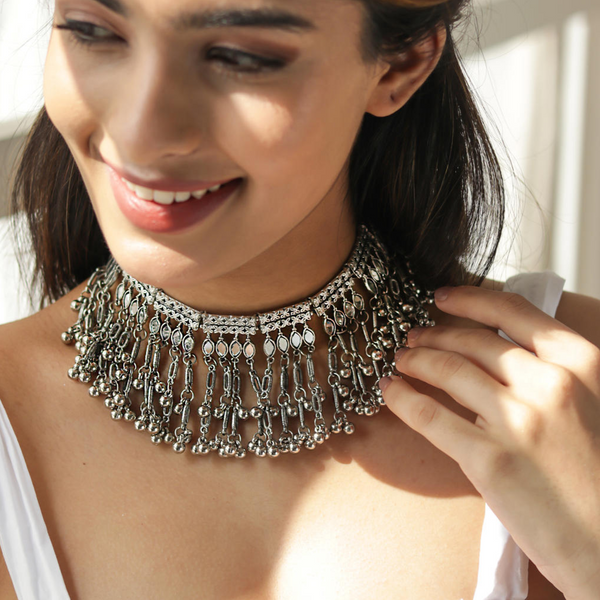 A woman wearing a silver oxidised bell-like choker necklace with a mirrored design.