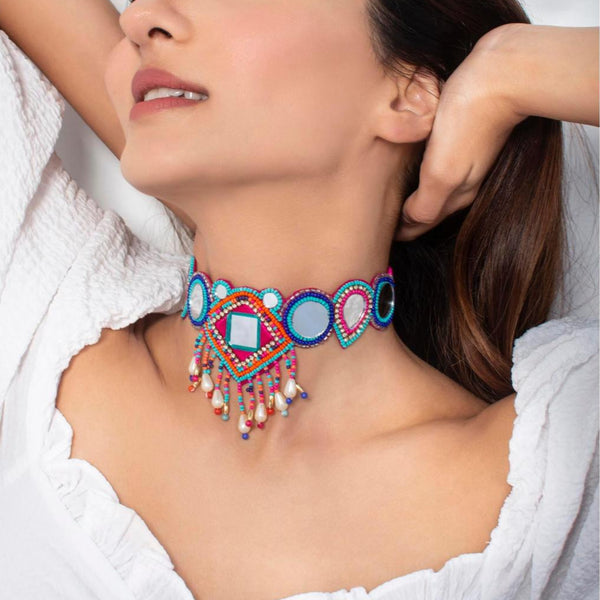 A person wearing a white outfit showcasing a multicolor beaded choker necklace with geometric patterns and mirror accents.