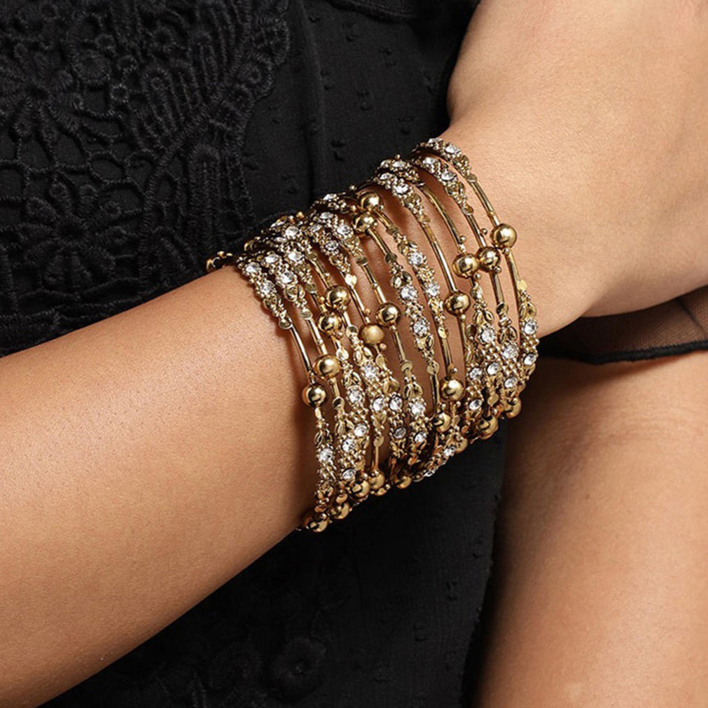 Model wearing Set of 12 gold-plated metal bangles with sparkling stones and beads. Perfect ethnic jewellery for weddings, parties & traditional celebrations.