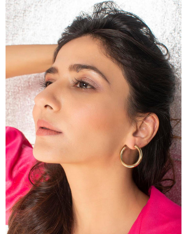 A woman wearing gold plated spherical hoop earrings.