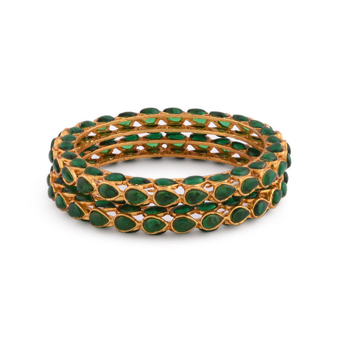 A set of two gold-plated bangles adorned with emerald stones and kundan work, displayed against a white background.