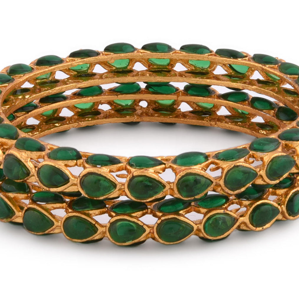 A set of two gold-plated bangles adorned with emerald stones and kundan work, displayed against a white background closeup