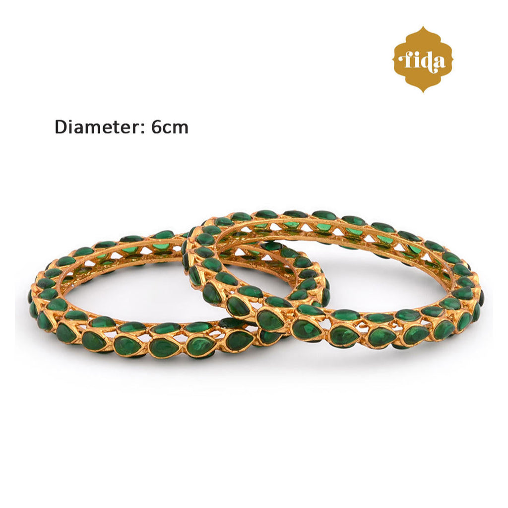A set of two gold-plated bangles adorned with emerald stones and kundan work, displayed against a white background dimension.