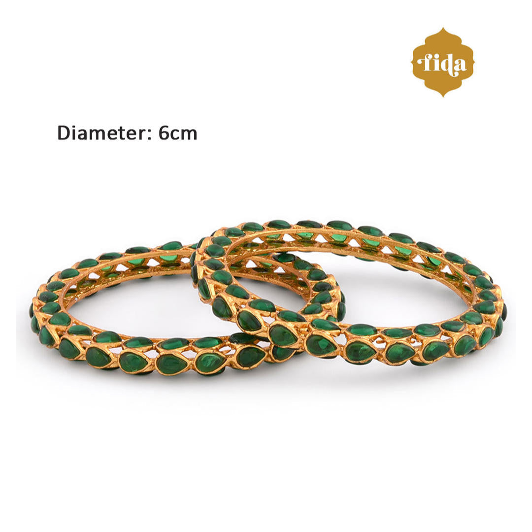 A set of two gold-plated bangles adorned with emerald stones and kundan work, displayed against a white background dimension.