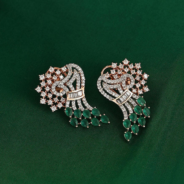 A pair of floral drop earrings with green beads and adorned with white and pink stones, displayed on a green surface with a wooden bowl and additional flowers in the background.