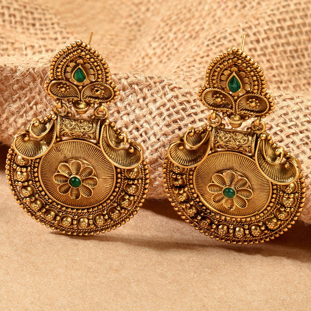 A pair of gold-plated antique floral design drop earrings with artificial stones on a textured background.