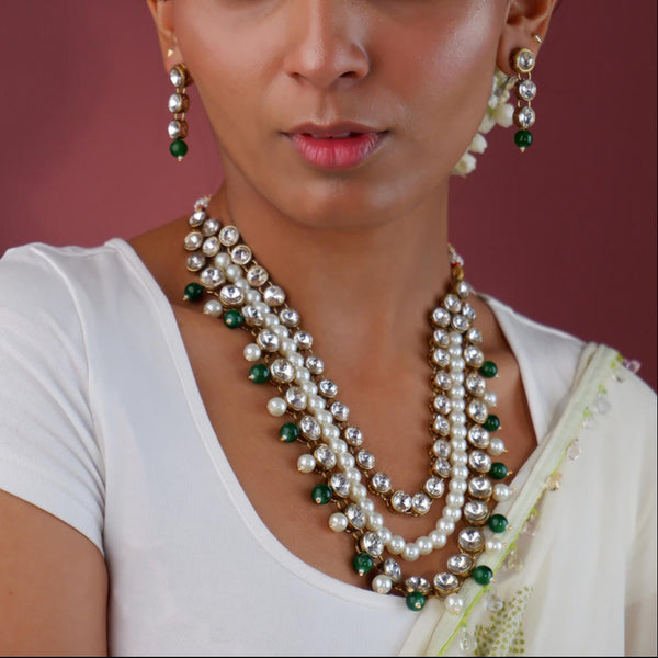 A woman wearing a gold plated necklace with green pearl beaded layers and matching earrings.
