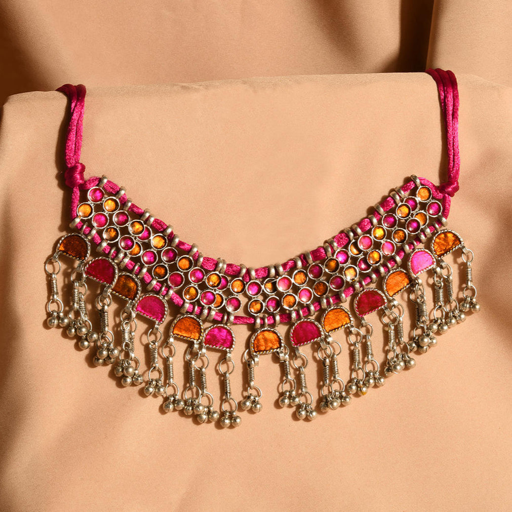 A pink and silver choker necklace with oxidised silver work and vibrant stone inlay, displayed against a beige background.