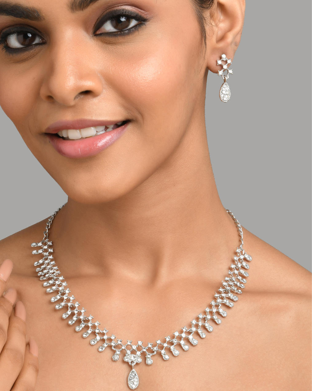 A woman wearing a silver plated jewellery set with intricate motifs and American diamond accents.