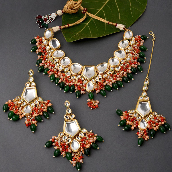 a gold plated jewellery set with red and green pearls and ornate Kundan work. The set includes a necklace, earrings, and a maangtikka.