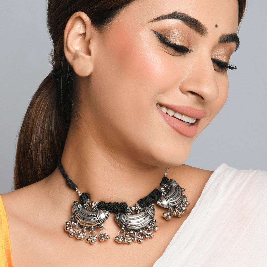 A woman wearing a choker necklace with oxidized silver detailing and black thread.