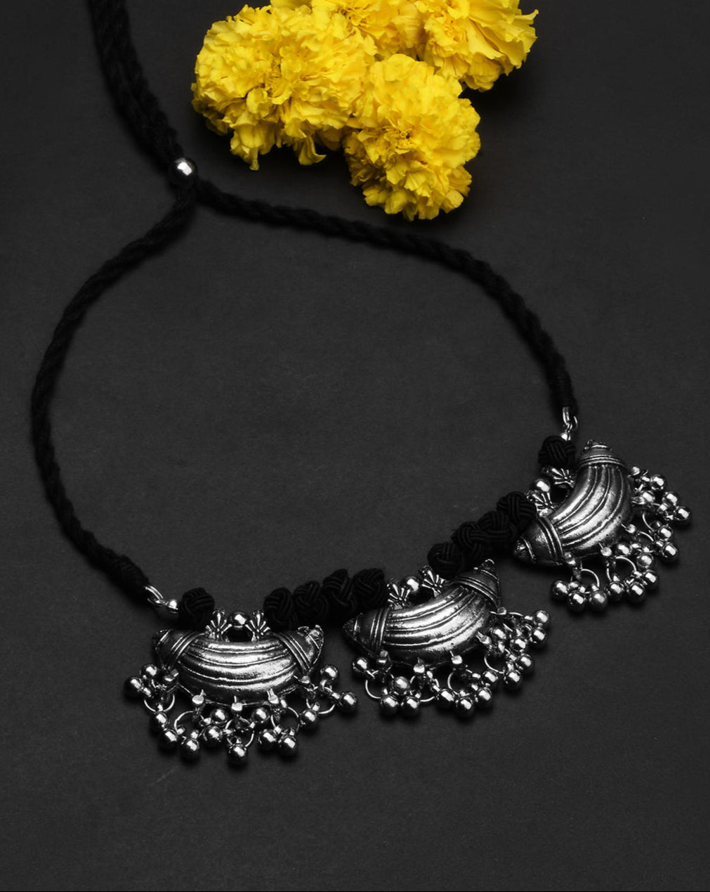 a choker necklace with oxidized silver detailing and black thread in a black background.