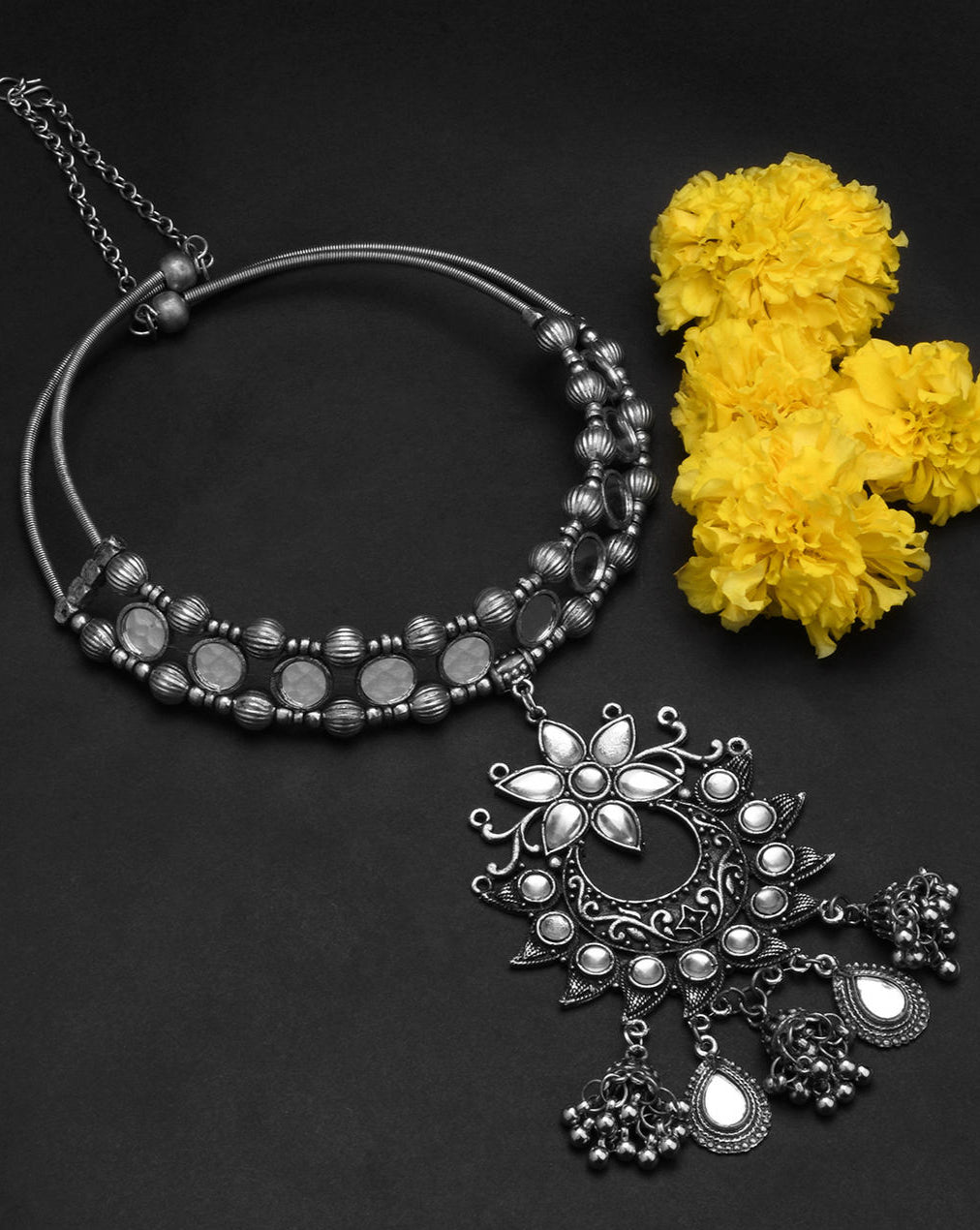Kundan sparkle choker necklace with intricate mirror work and a large pendant adorned with Kundan stones, along with ghungroo drops on black background with flowers