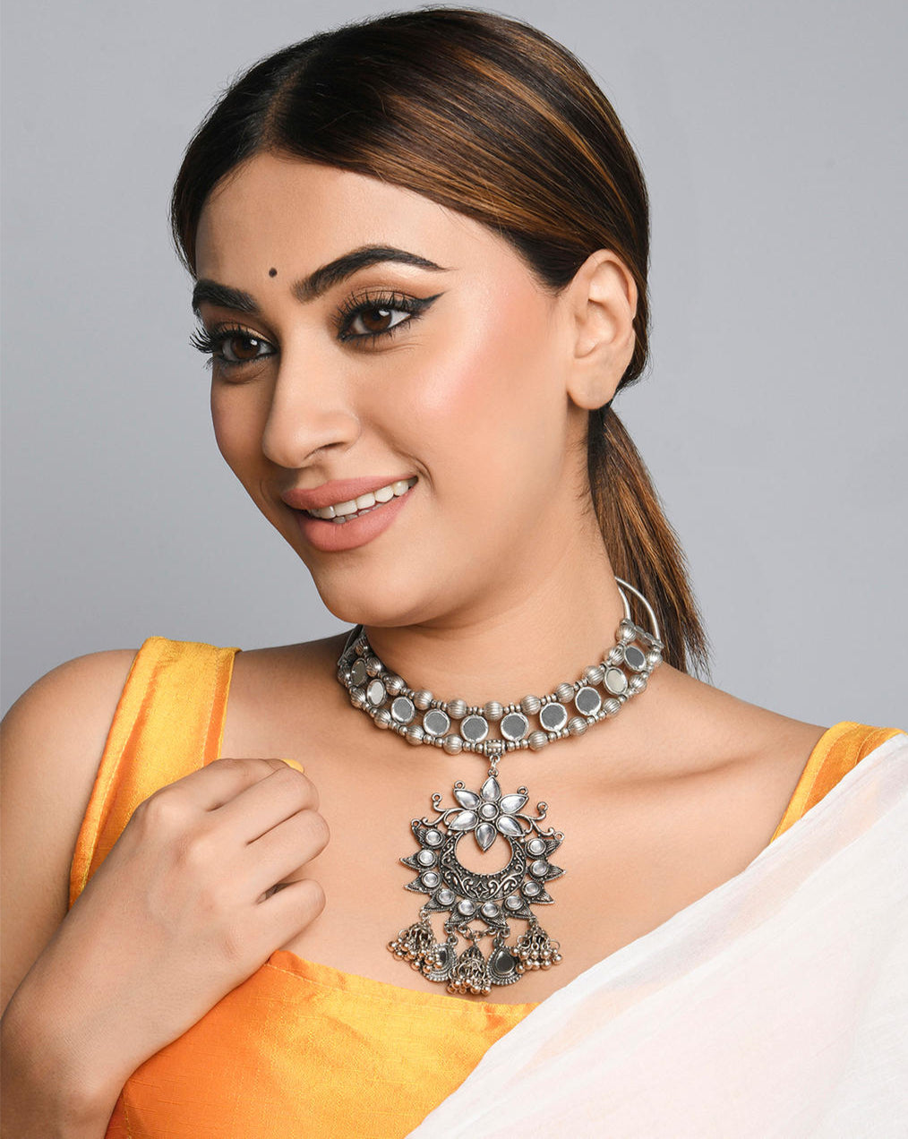 Model wearing Kundan sparkle choker necklace with intricate mirror work and a large pendant adorned with Kundan stones, along with ghungroo drops.