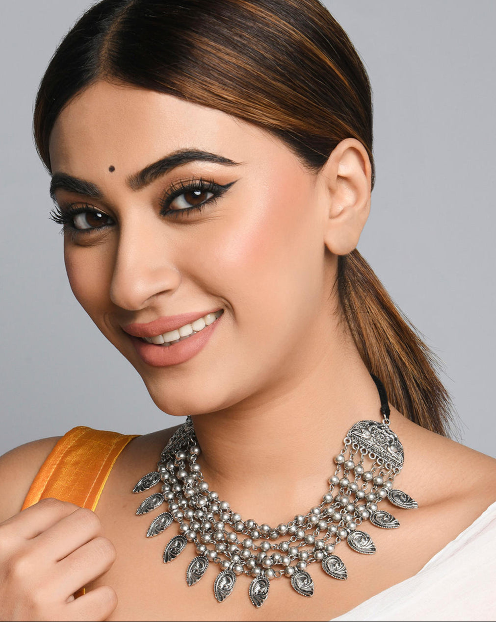 A woman wearing a multi-strand choker necklace with oxidized silver beads and embossed peacock charms.