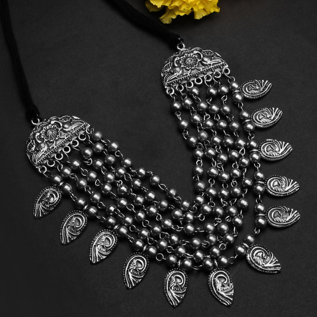 a multi-strand choker necklace with oxidized silver beads and embossed peacock charms on a black background