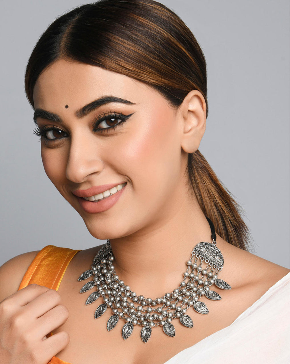 A woman wearing a multi-strand choker necklace with oxidized silver beads and embossed peacock charms.