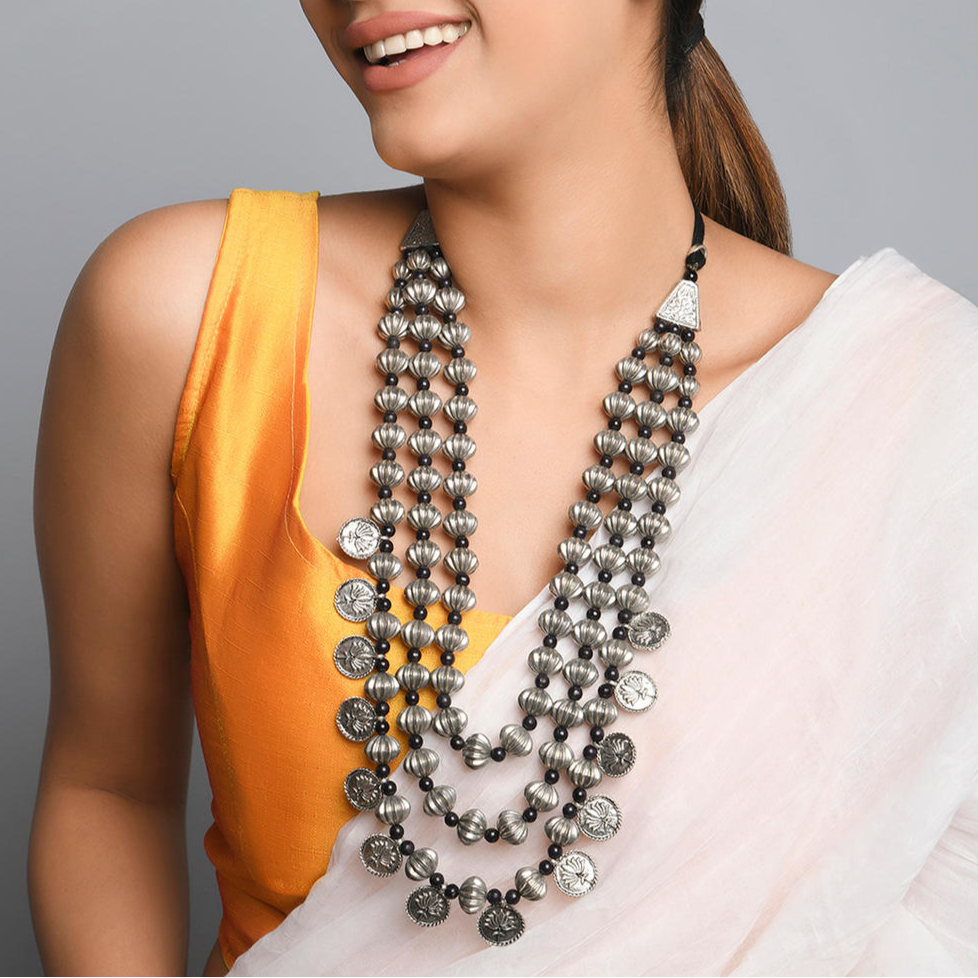 A woman wearing a white saree with fida's multilayered silver coin necklace and an orange blouse.