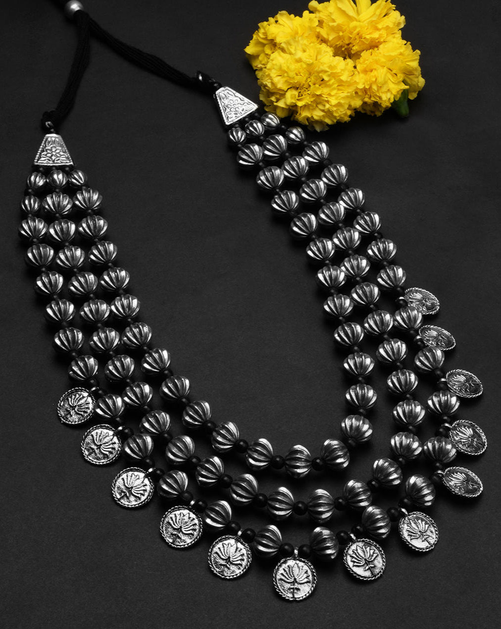 multilayered silver coin necklace with black background with studio setup and yellow flower