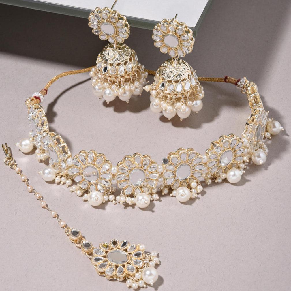a traditional pearl and mirror kundan jewellery set which includes a choker necklace, earrings, and a maang tikka. The set is gold-plated with white artificial stones.