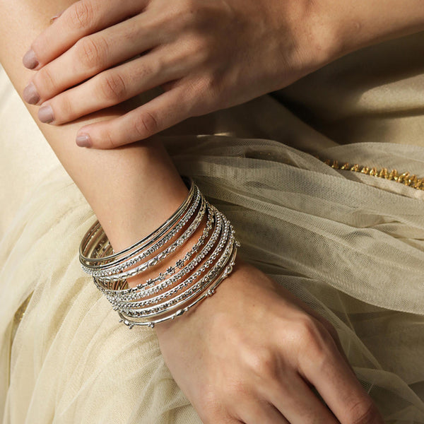 Women's forearm adorned with a set of silver-plated bangles featuring stones and beads, wearing a light-colored garment.