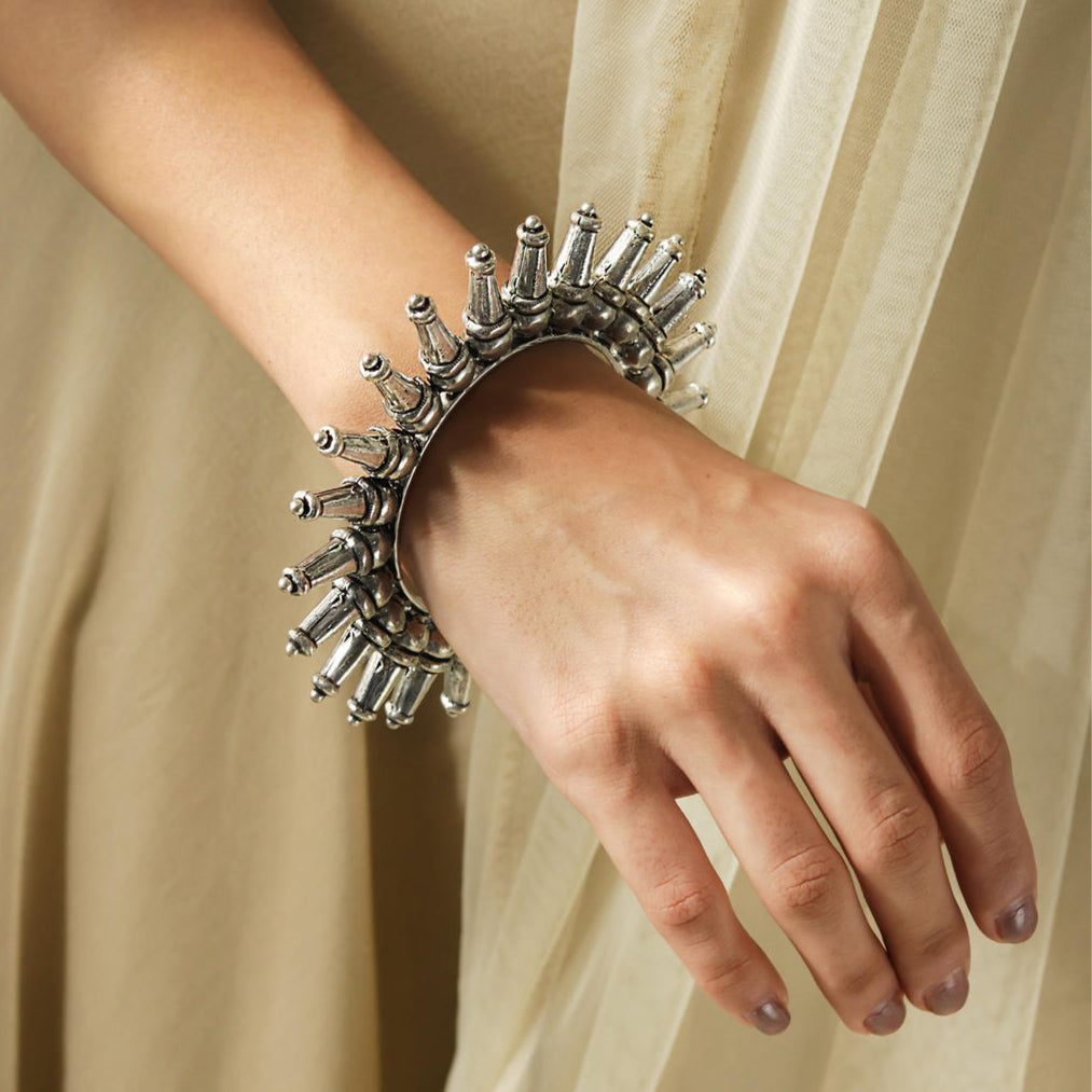 A silver-plated oxidized tribal kada bangle with a rays pattern, worn on a women's wrist.