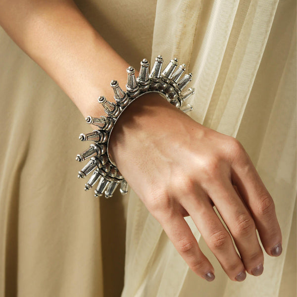 A silver-plated oxidized tribal kada bangle with a rays pattern, worn on a women's wrist.