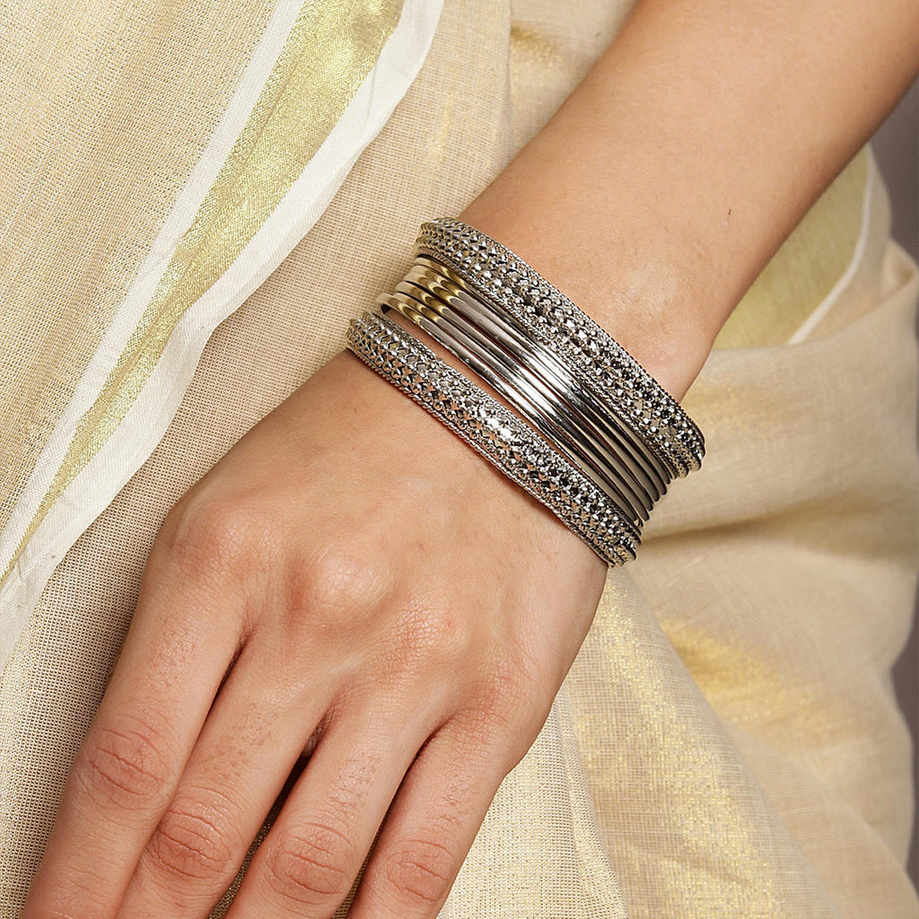 A women's wrist wearing a set of silver-plated bangles with intricate designs, displayed against a light background.