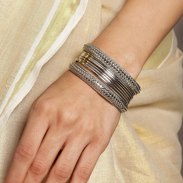 A women's wrist wearing a set of silver-plated bangles with intricate designs, displayed against a light background.