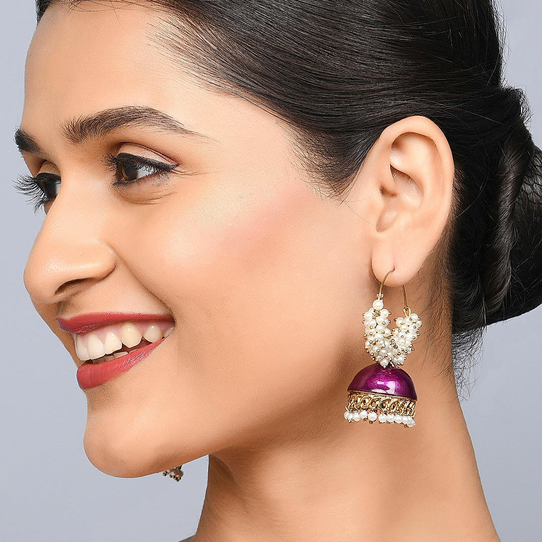 A woman smiling and wearing a silver-colored hoop jhumka earring with purple meenakari and pearl studs.
