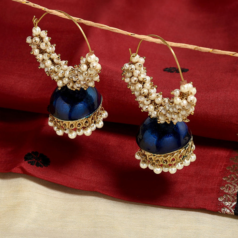 A pair of gold-plated navy blue enamelled and pearl accented hoop jhumka earrings displayed against a red fabric background.