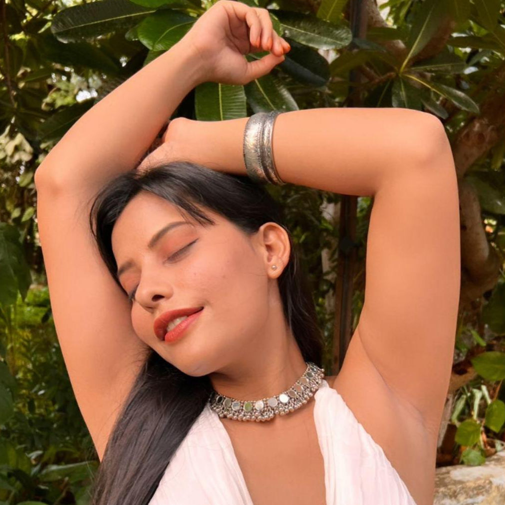 A model wearing a white top and showcasing a silver oxidized choker necklace with mirrored ghungroo details.