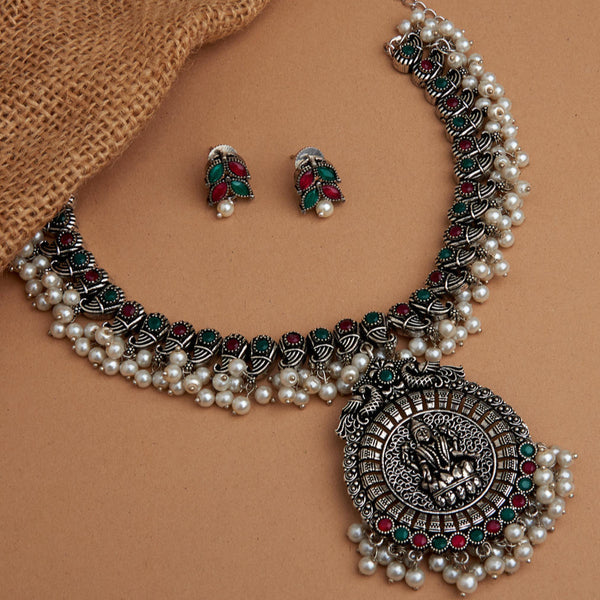 A silver-plated oxidised temple jewellery set with white pearls and green and red stones, featuring a detailed pendant and a pair of earrings.