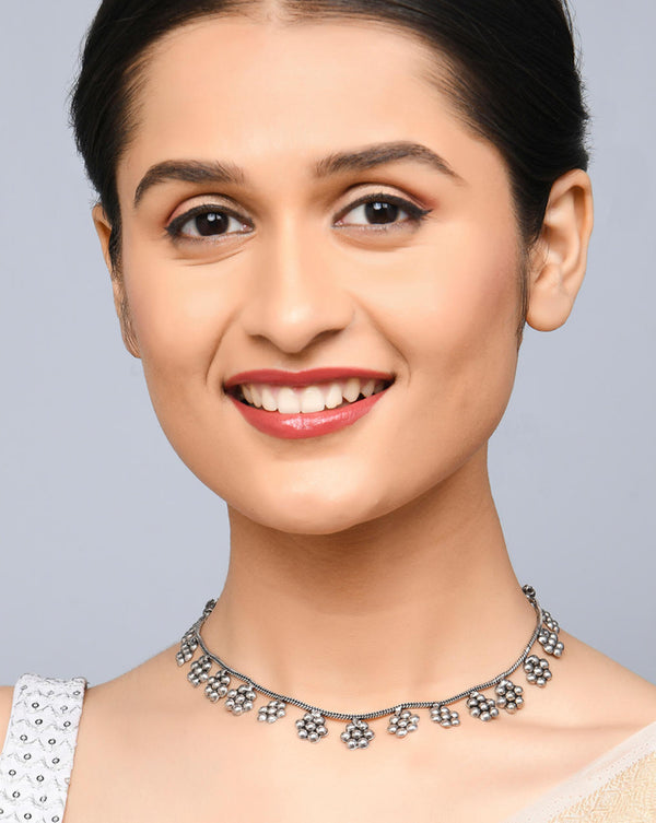A woman smiling and showcasing a silver-toned floral choker necklace which has a vintage finish.