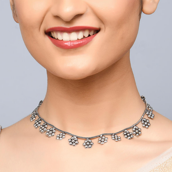 A woman smiling and showcasing a silver-toned floral choker necklace which has a vintage finish.